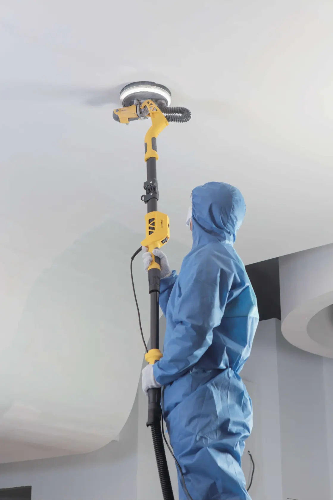 STANLEY SW75-BR lijadora de pared usada por persona en traje azul, lijando techo blanco, fotografía lateral
